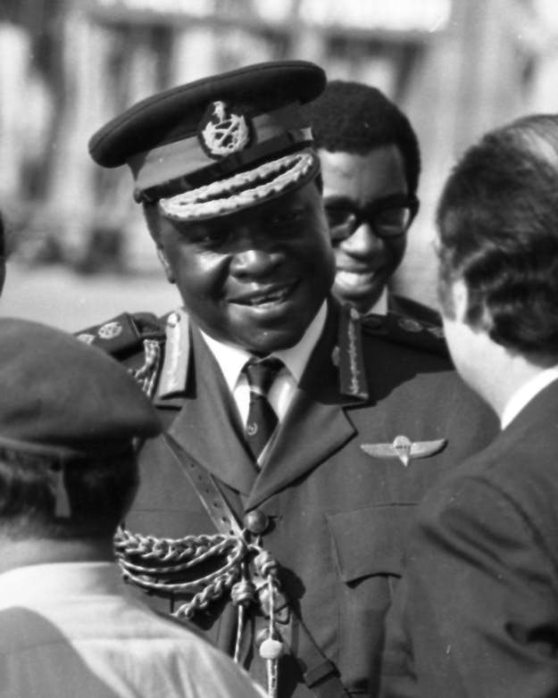 Een lachende Idi Aban staat in uniform tegenover een aantal bestuurders. Een lachende Idi Aban staat in uniform tegenover een aantal bestuurders.