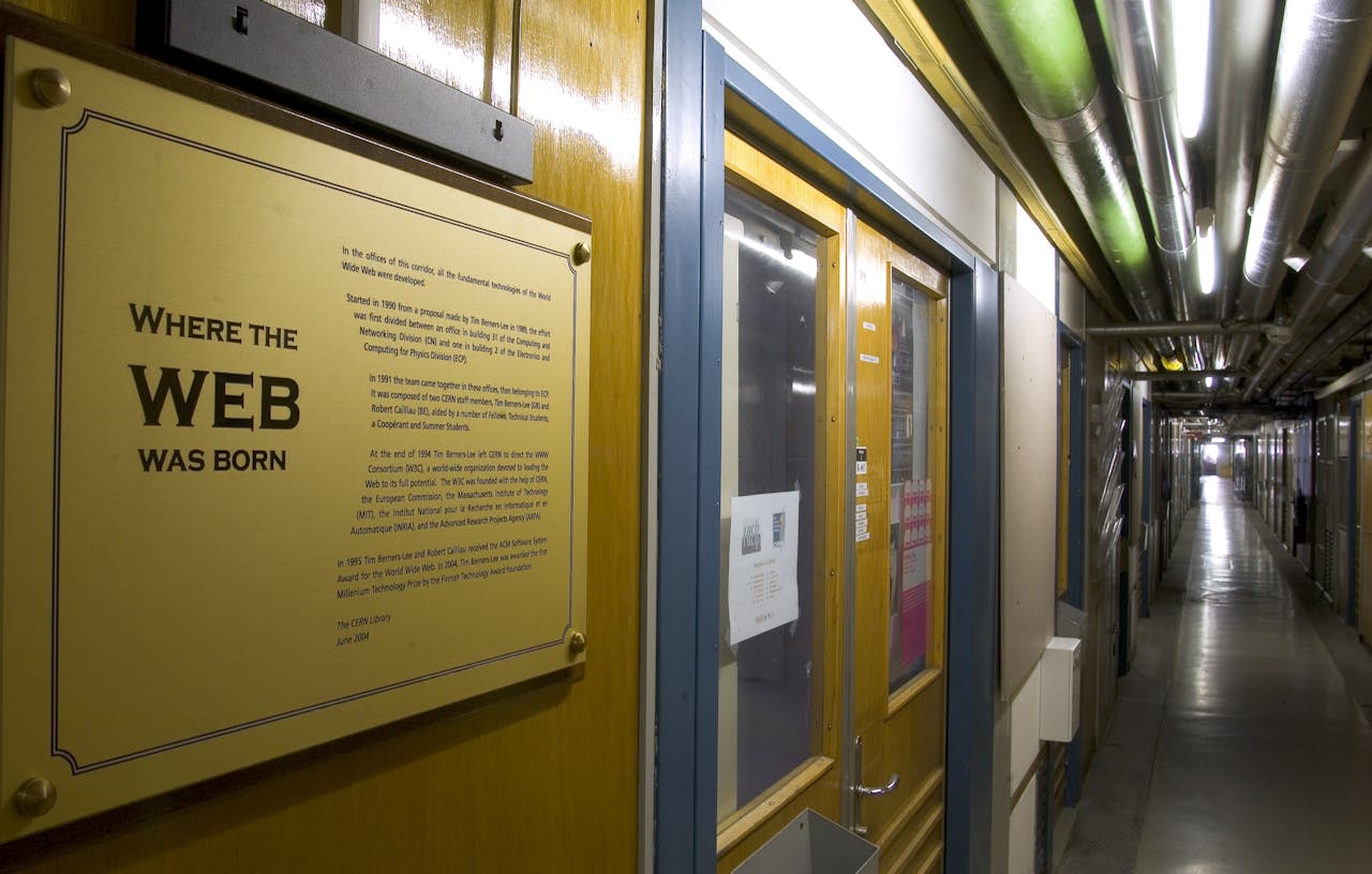 Een lange gang met naast een dubbele deur een grote gouden plaquette met daarop  de tekst 'Where the web was born'.