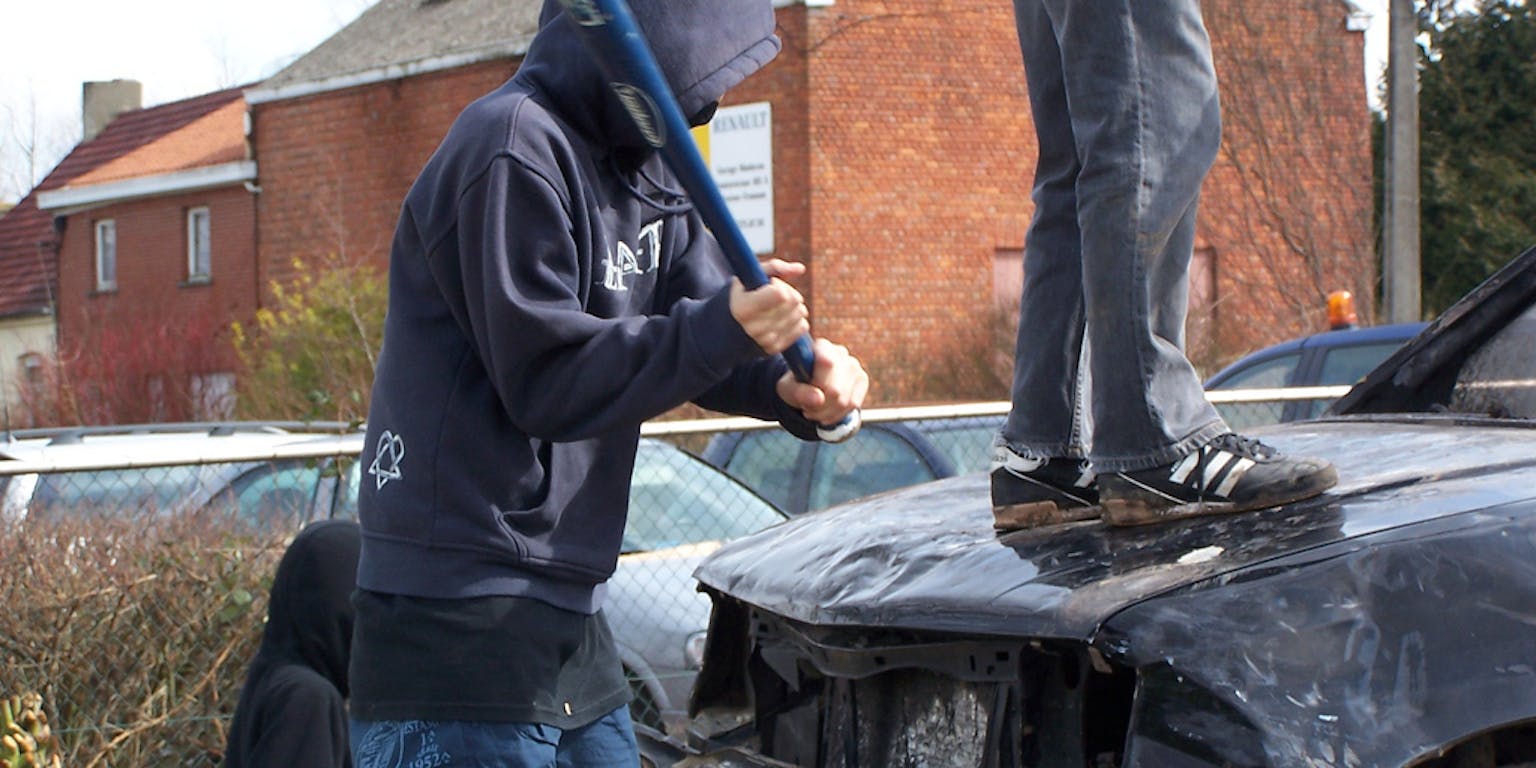 Twee personen slaan met een honkbalknuppel tegen een beschadigde zwarte auto.