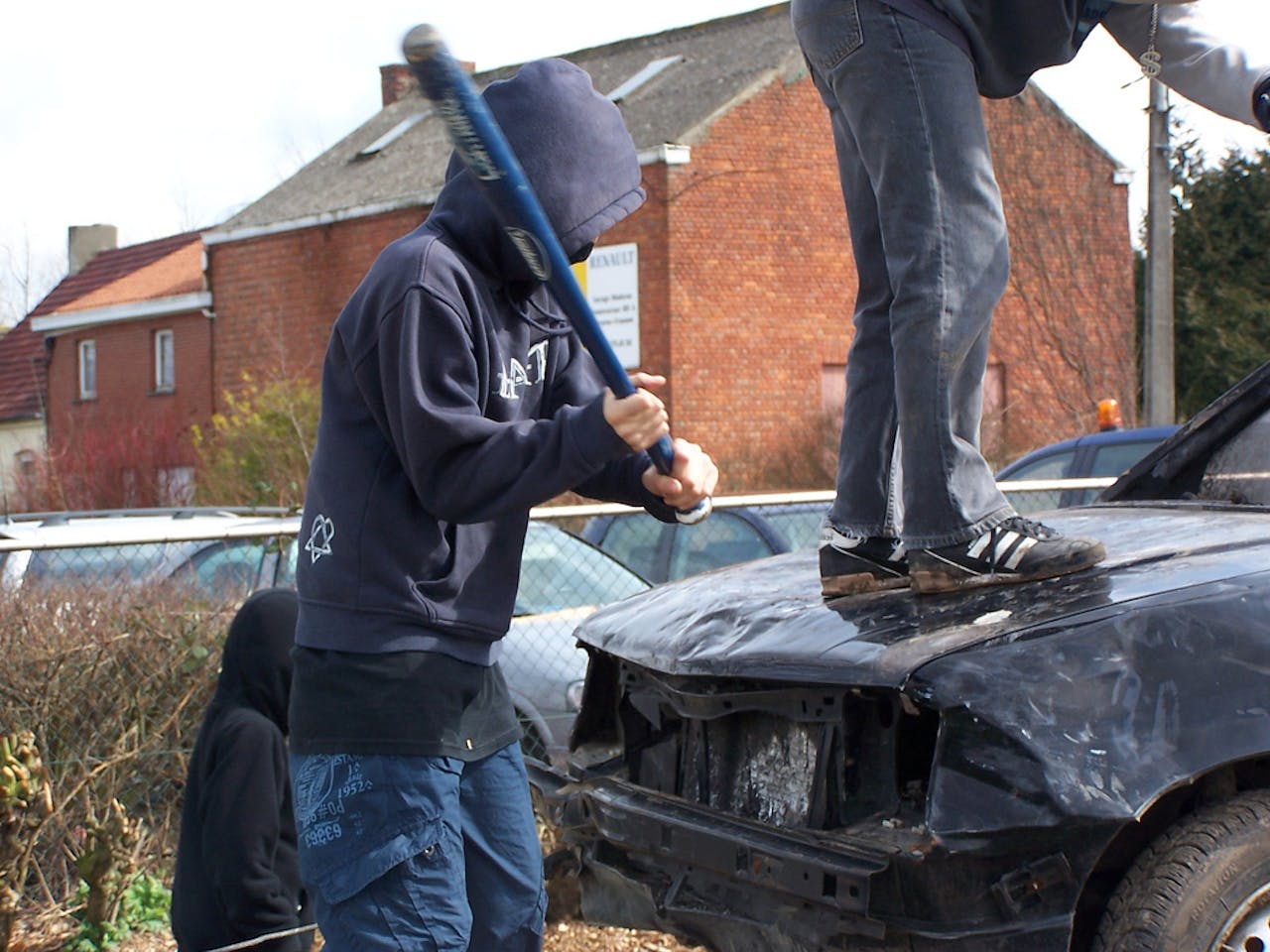 Twee personen slaan met een honkbalknuppel tegen een beschadigde zwarte auto.