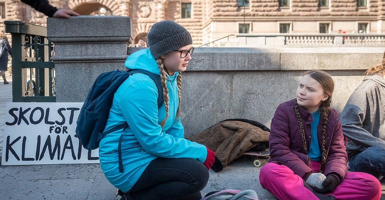 Twee jonge meisjes zitten op de grond naast een bord voor klimaatverandering.