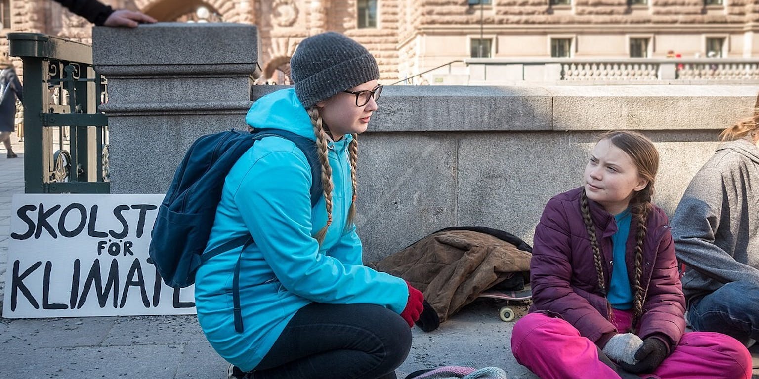 Twee jonge meisjes zitten op de grond naast een bord voor klimaatverandering.