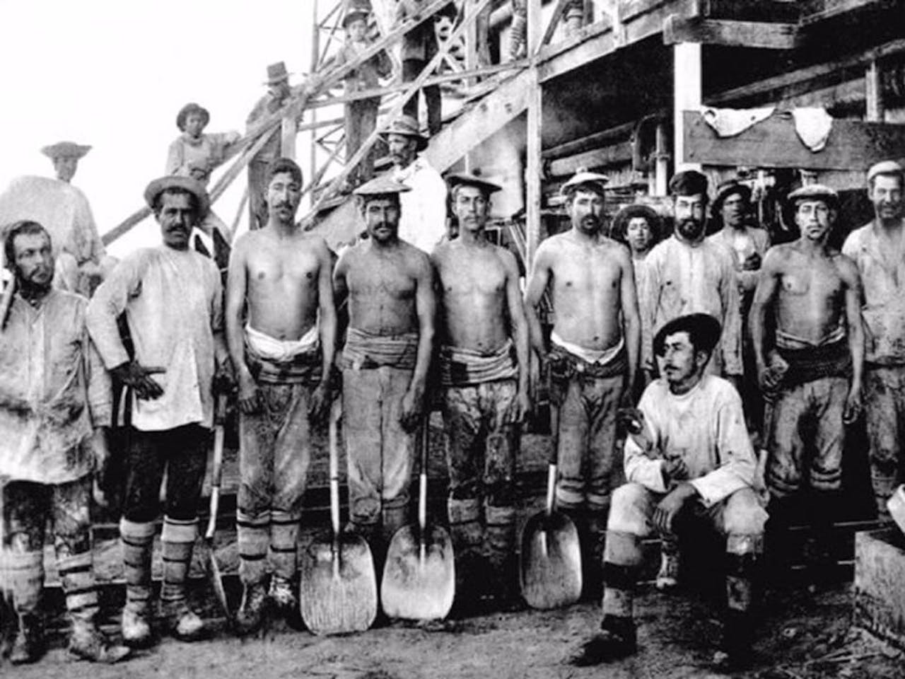 Een groep mijnwerkers met schoppen staan voor een gebouw.