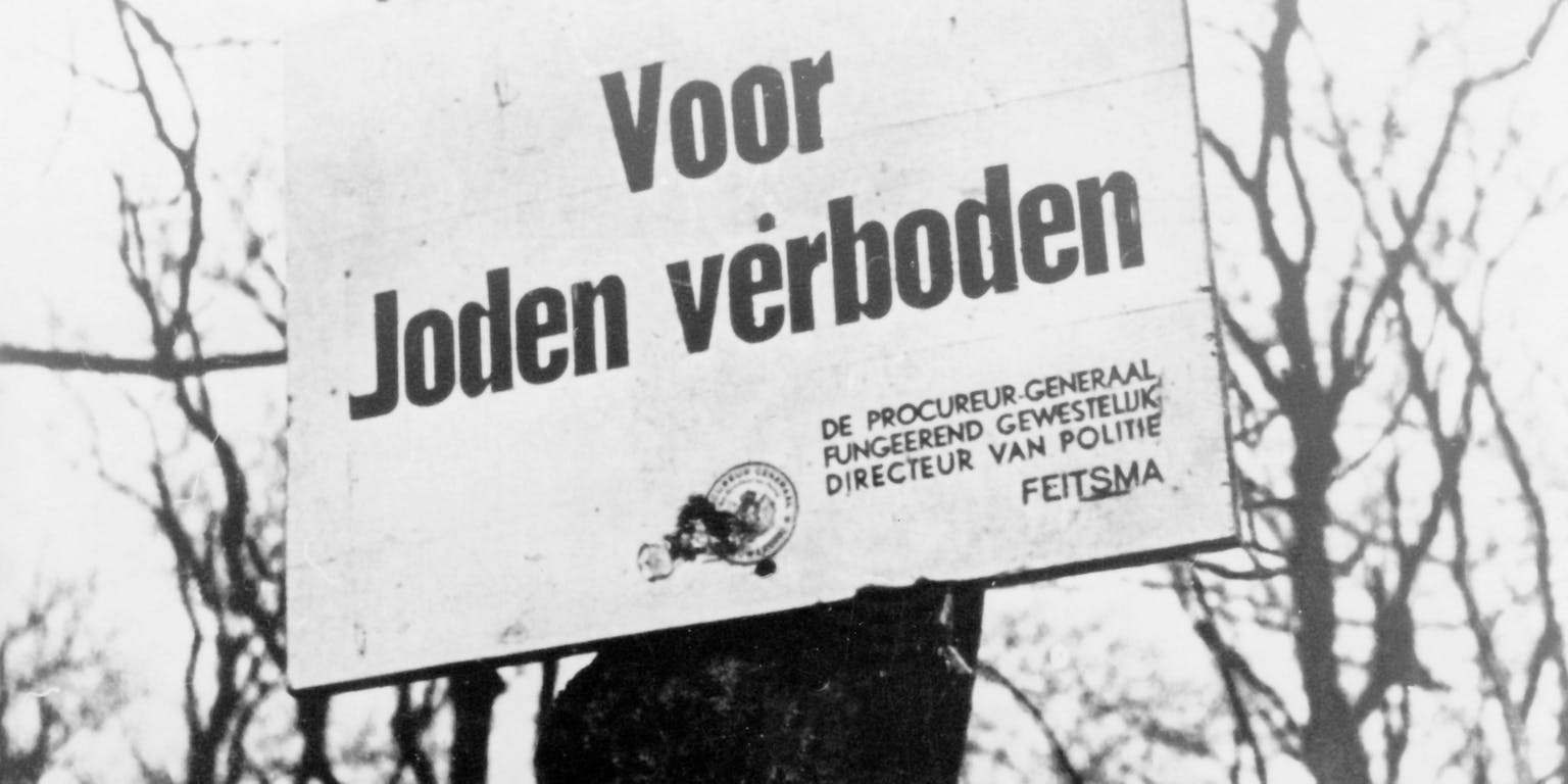 Een zwart-witfoto van een bord met de tekst 'voor joden verboden'.