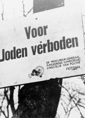 Een zwart-witfoto van een bord met de tekst 'voor joden verboden'.