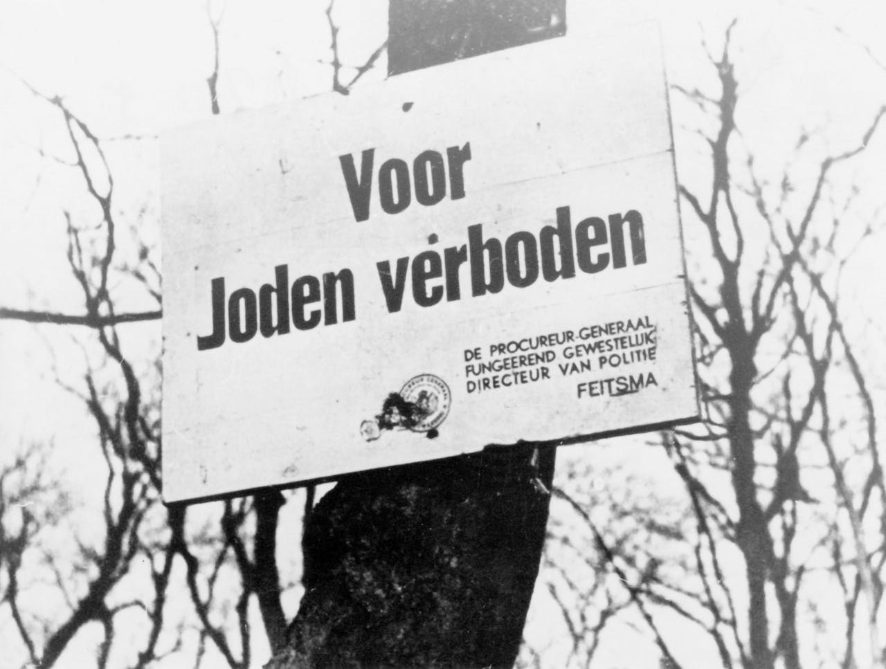 Een zwart-witfoto van een bord met de tekst 'voor joden verboden'.