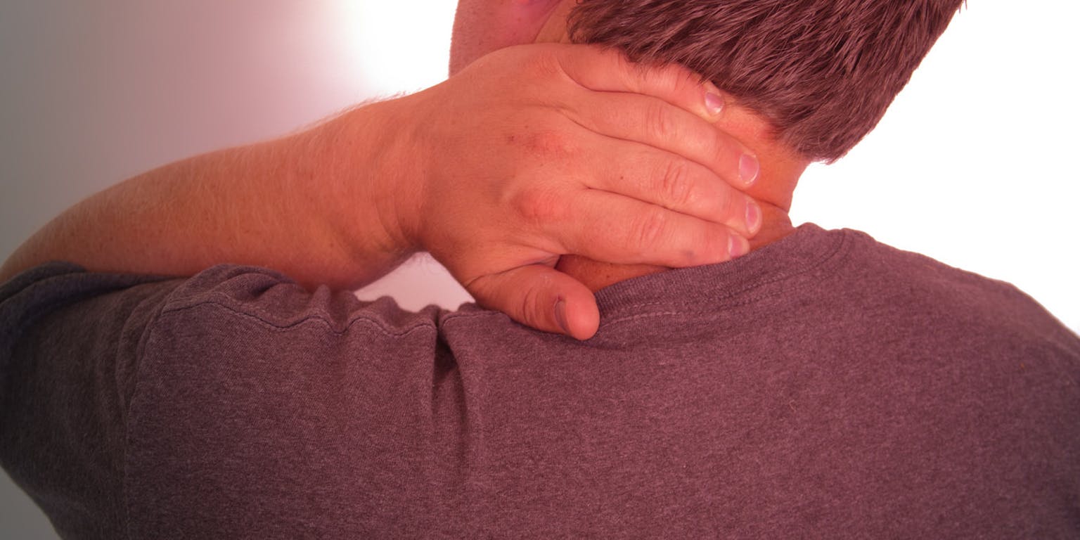 Een man met nekpijn. Hij heeft zijn hand in zijn nek vast.