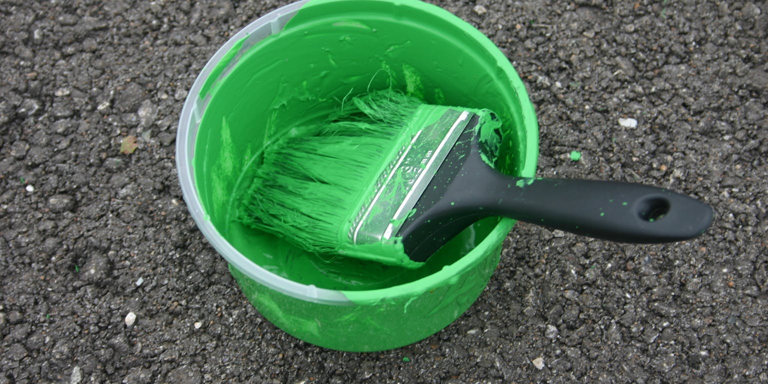 Een bakje groene verf met een grote blokkwast erin.