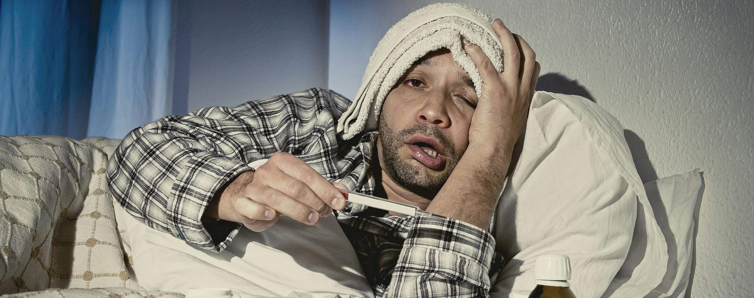 Een man ligt in bed met een thermometer en medicijnen.
