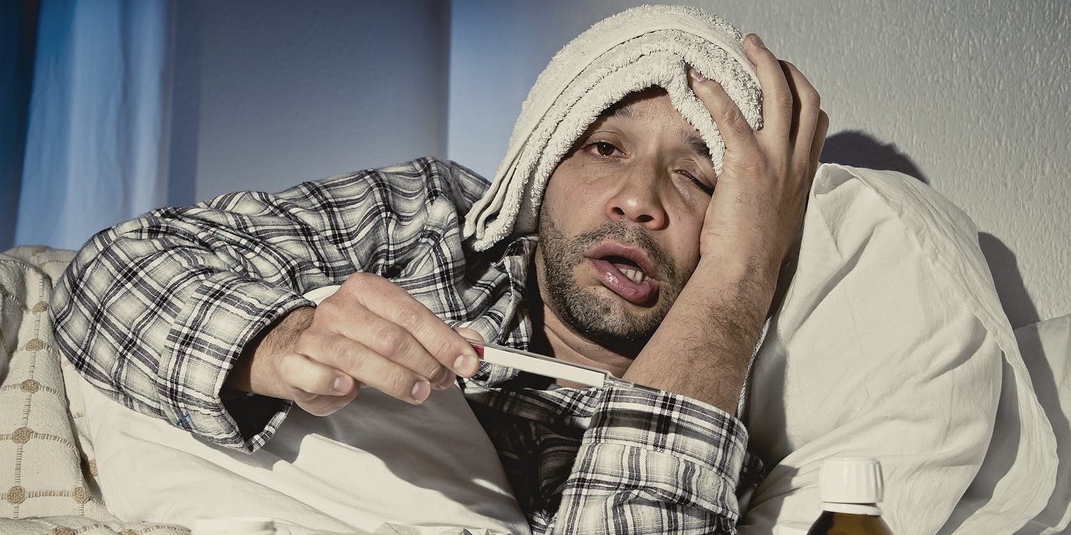Een man ligt in bed met een thermometer en medicijnen.