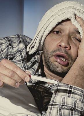 Een man ligt in bed met een thermometer en medicijnen.