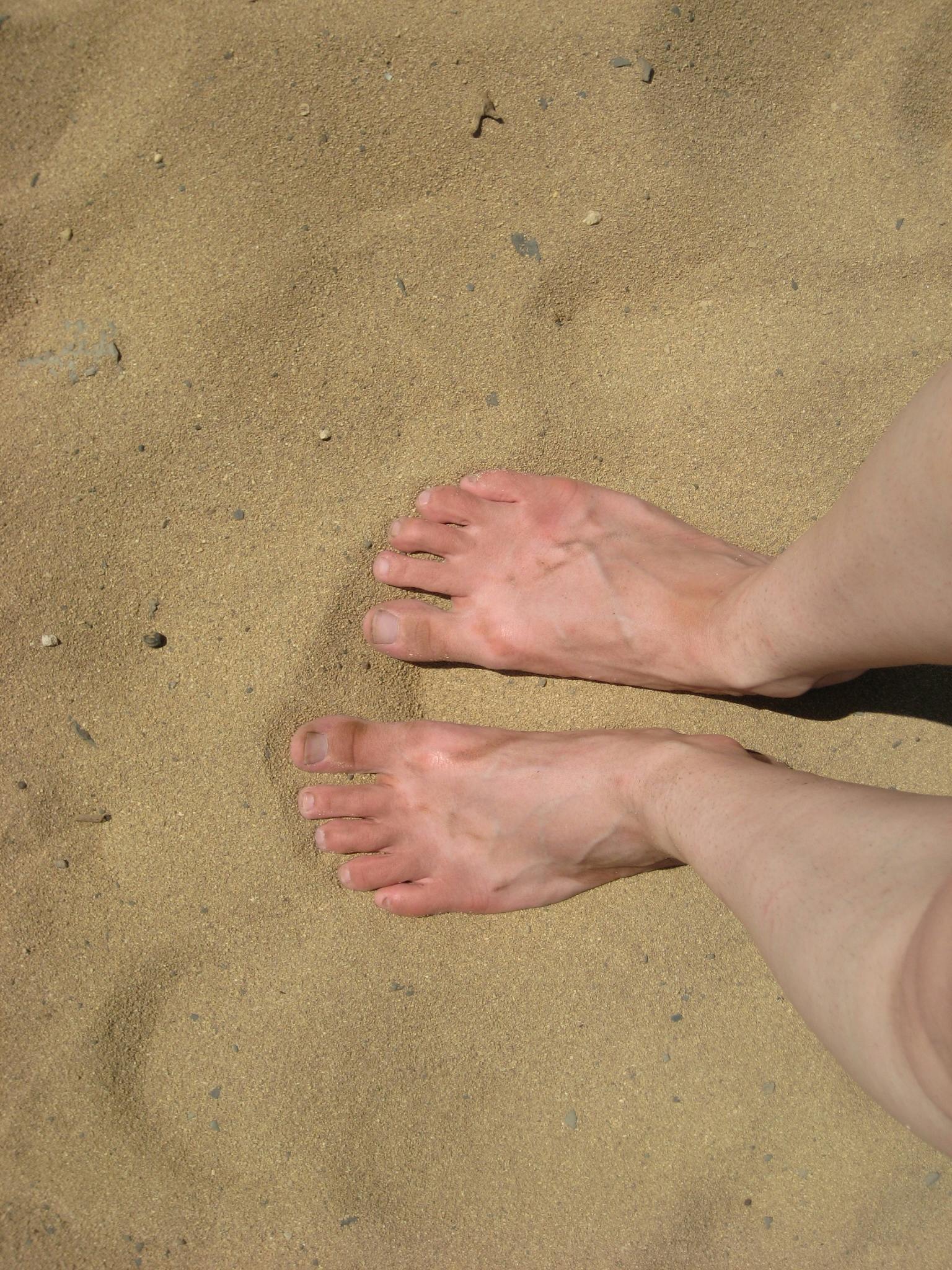 De voeten van een persoon staan in het zand.