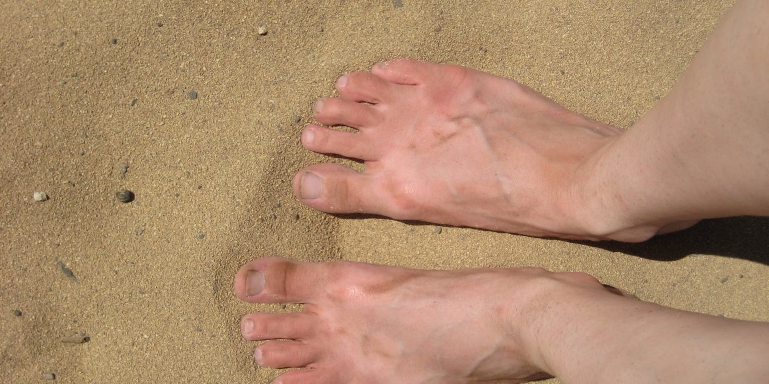 De voeten van een persoon staan in het zand.