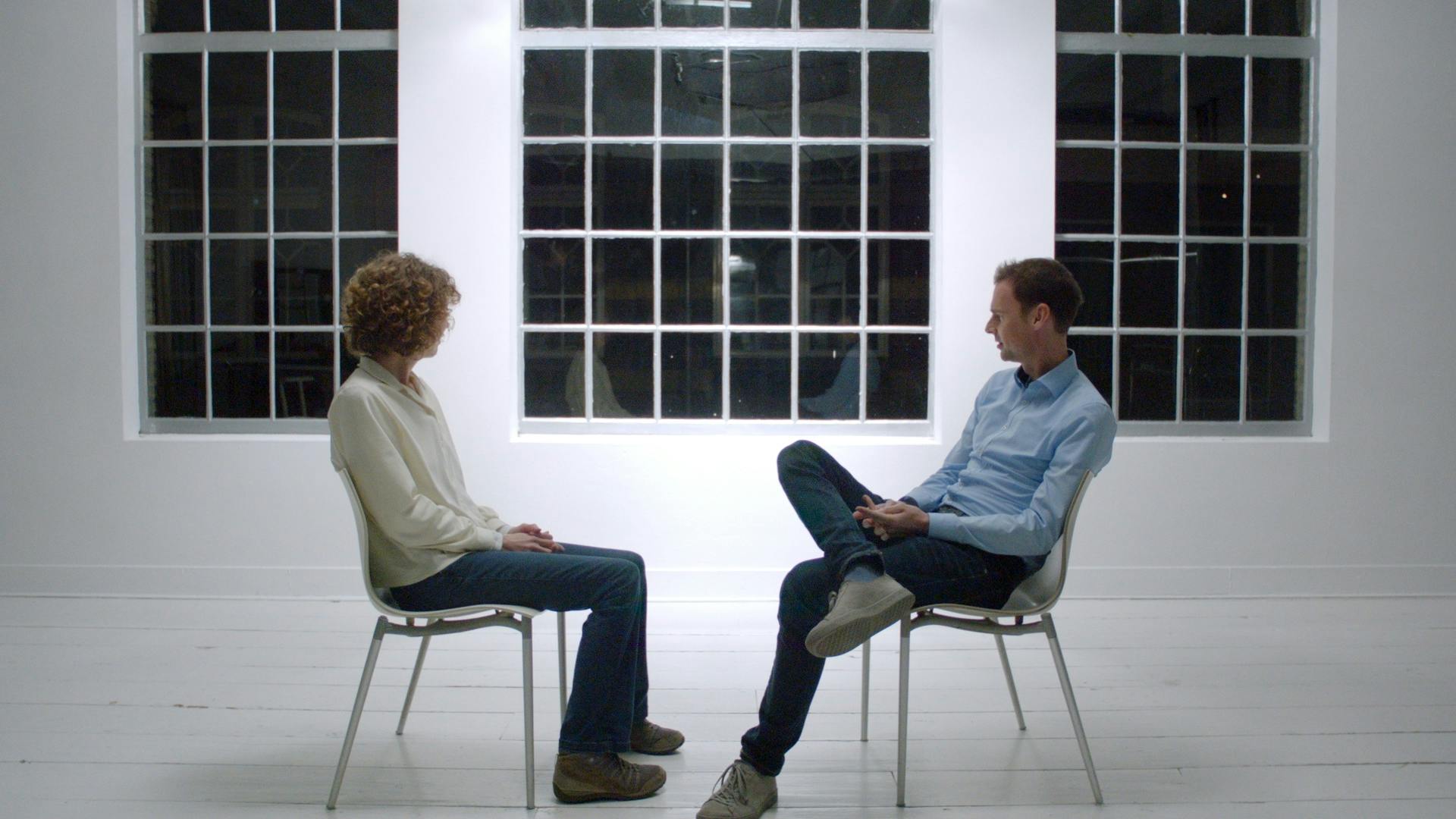 Twee mensen zitten op stoelen voor een raam.