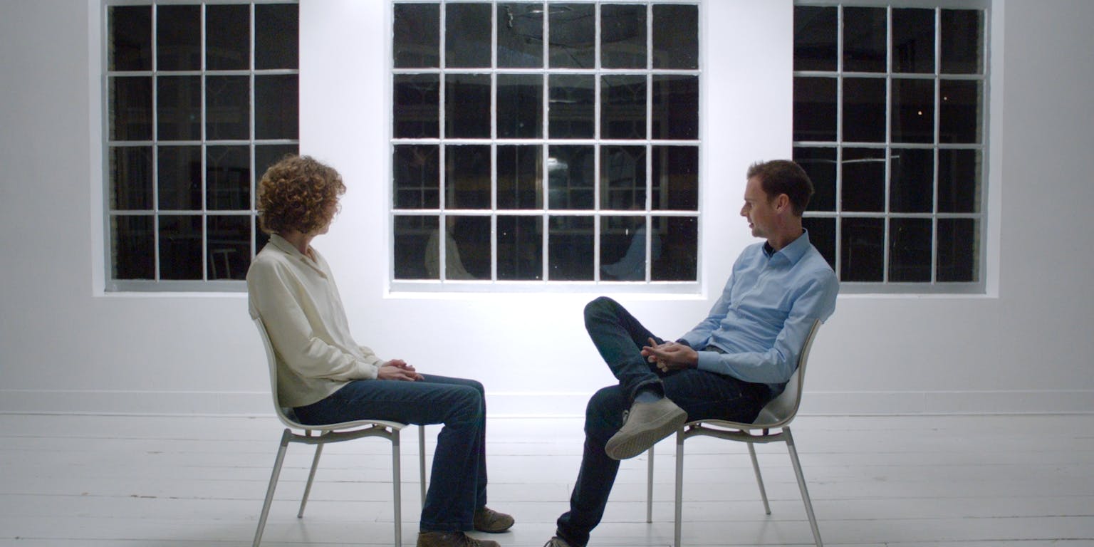 Twee mensen zitten op stoelen voor een raam.