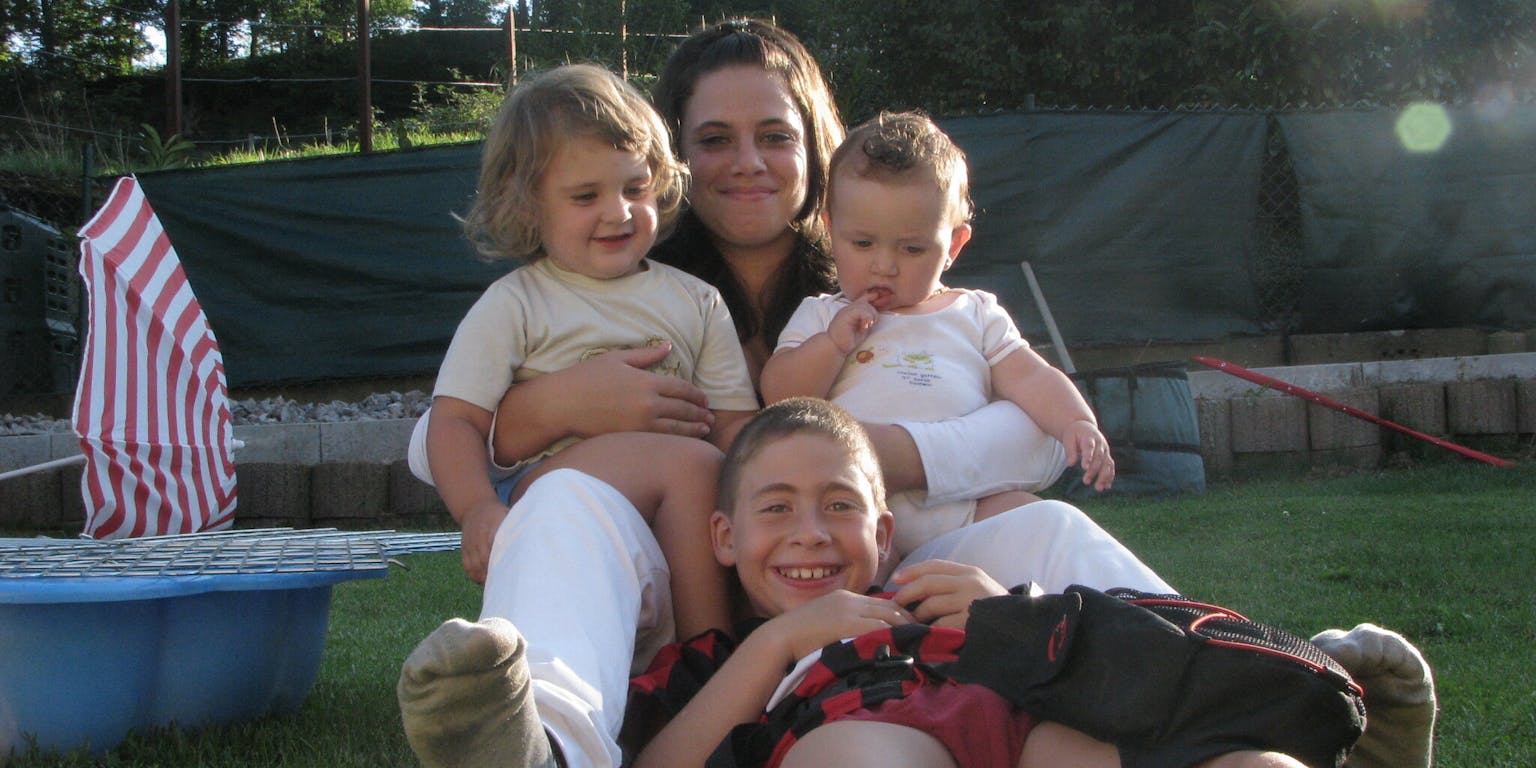 Een vrouw en drie kinderen zitten in het gras.