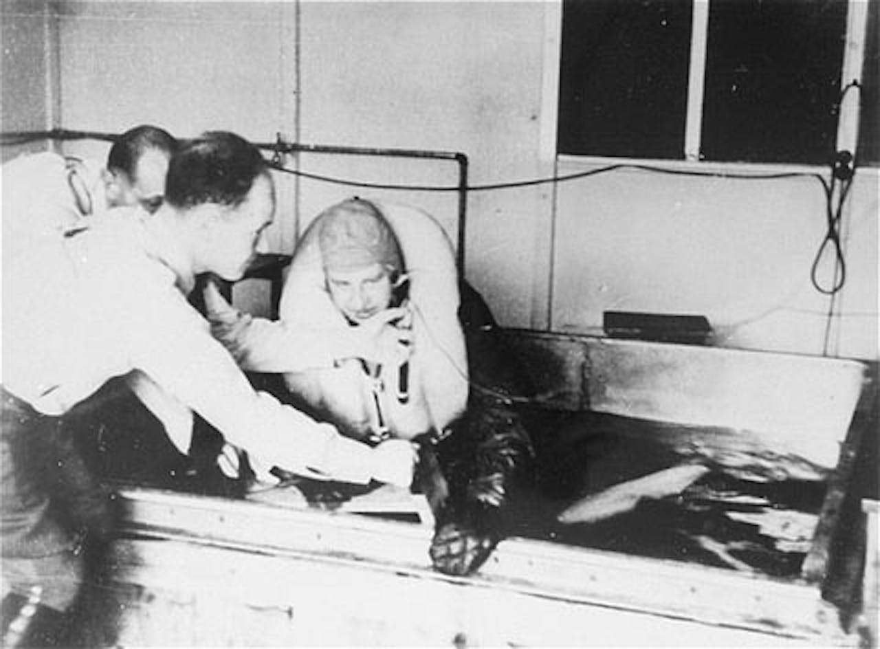 Afbeelding van experiment in concentratiekamp waarin twee mannen en derde man in een pilotenpak in een ijsbad helpt.