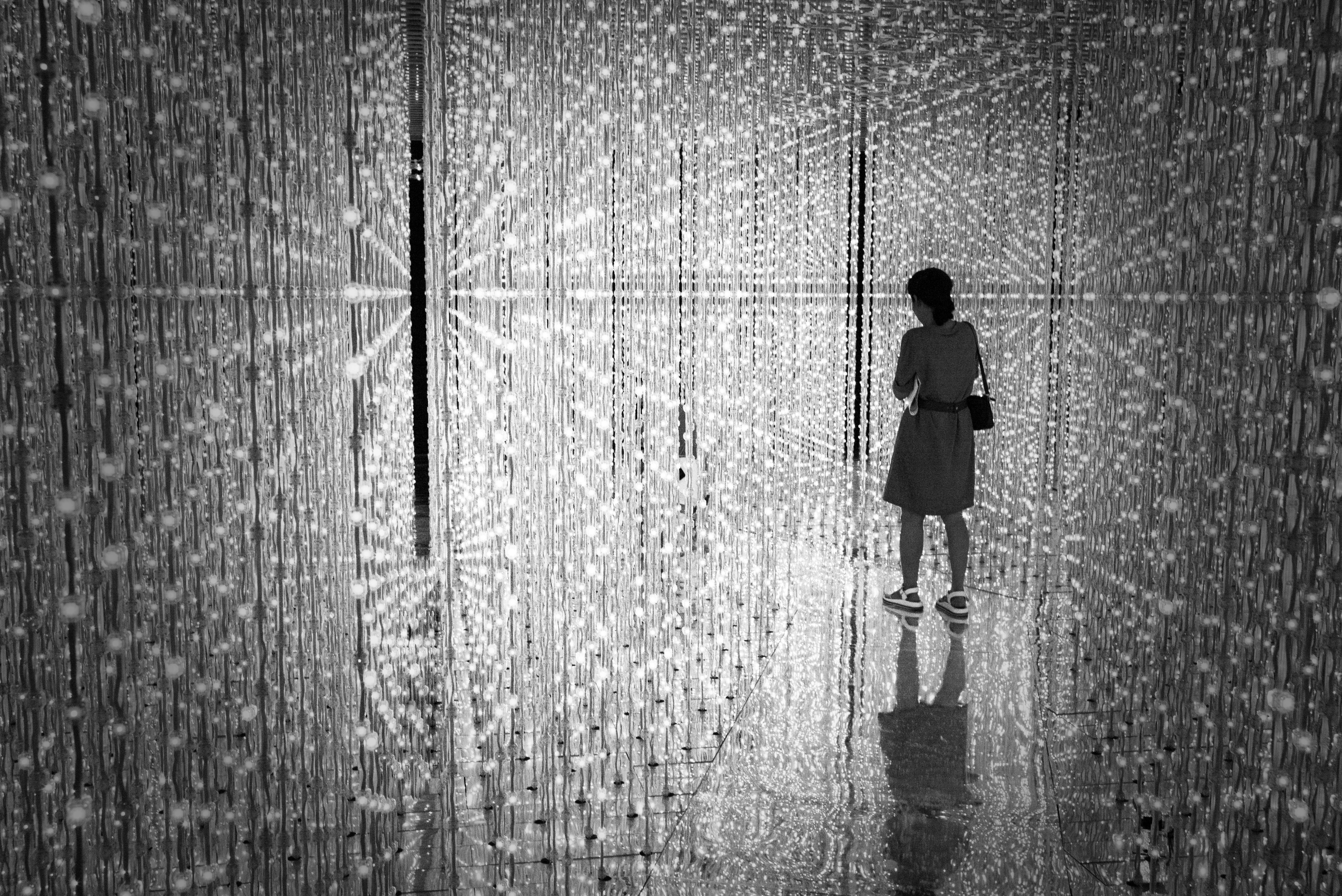 Een vrouw staat in een oneindige ruimte vol glitteringen. De ruimte is onderdeel van teamLab Planets TOKYO.