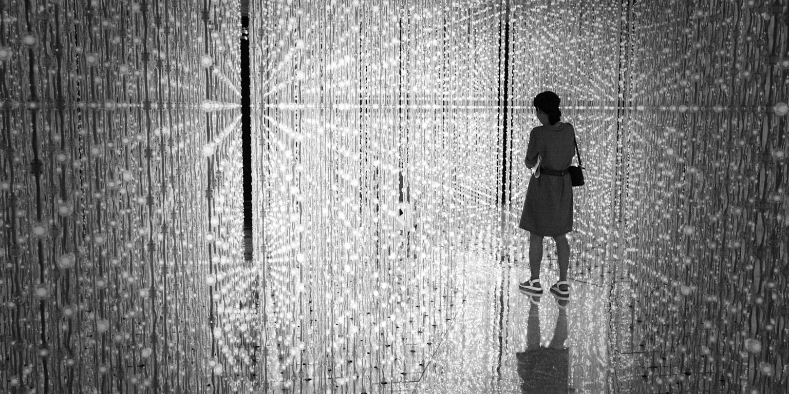 Een vrouw staat in een oneindige ruimte vol glitteringen. De ruimte is onderdeel van teamLab Planets TOKYO.