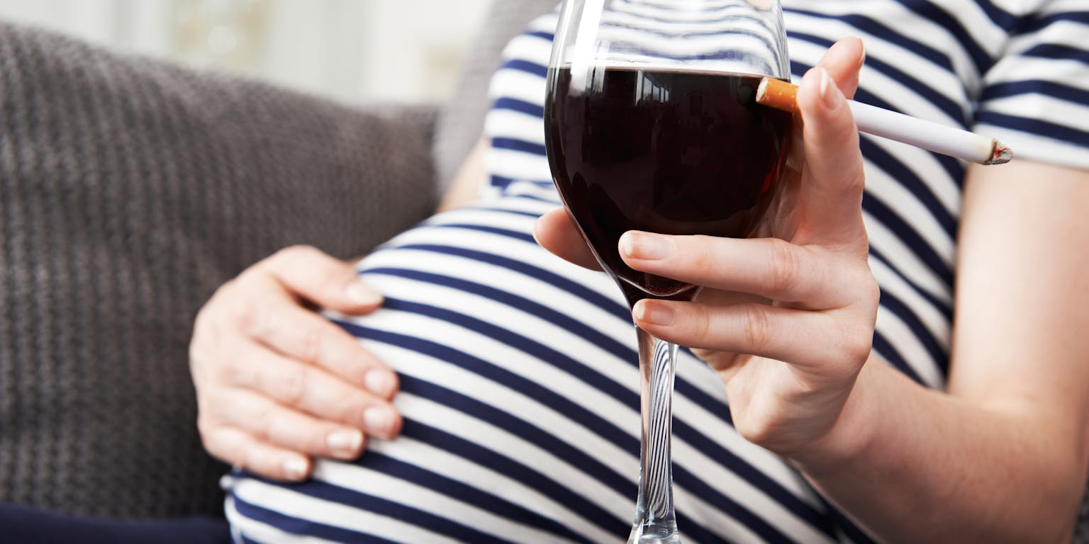 Een zwangere vrouw die een glas wijn vasthoudt.