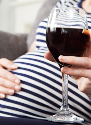 Een zwangere vrouw die een glas wijn vasthoudt.