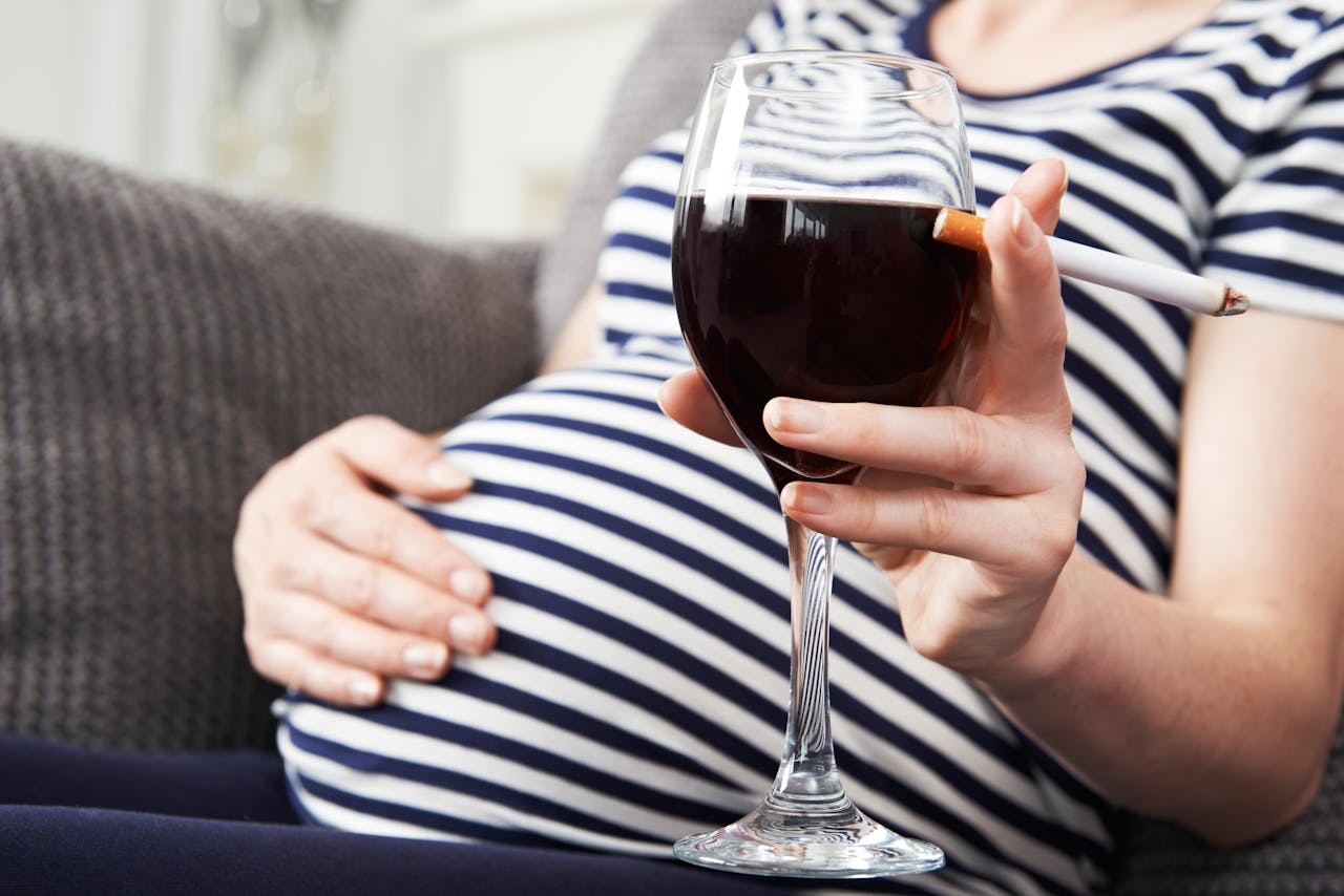 Een zwangere vrouw die een glas wijn vasthoudt.