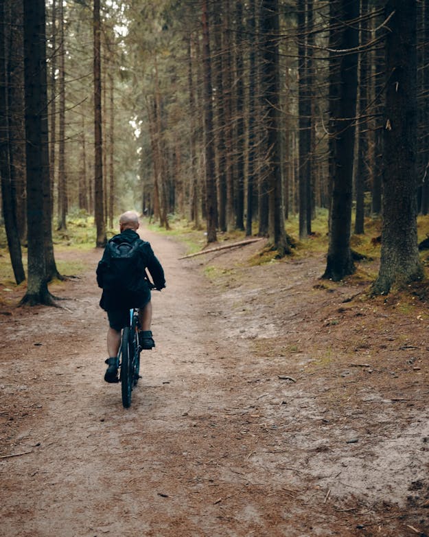 Achteraanzicht van oudere man op een mountainbike in een bos Achteraanzicht van oudere man op een mountainbike in een bos