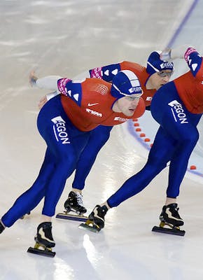 Drie schaatsers op een baan.