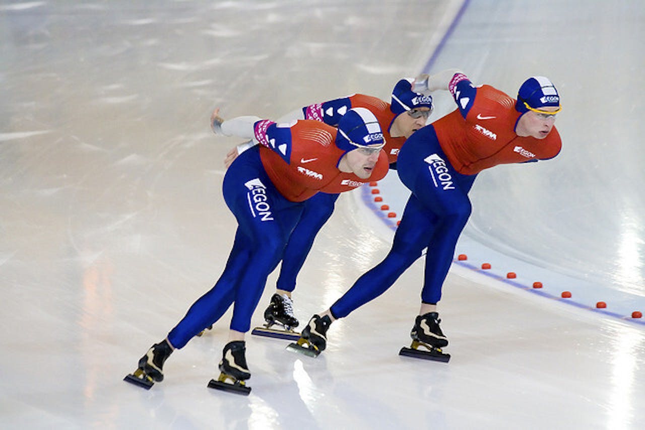 Drie schaatsers op een baan.