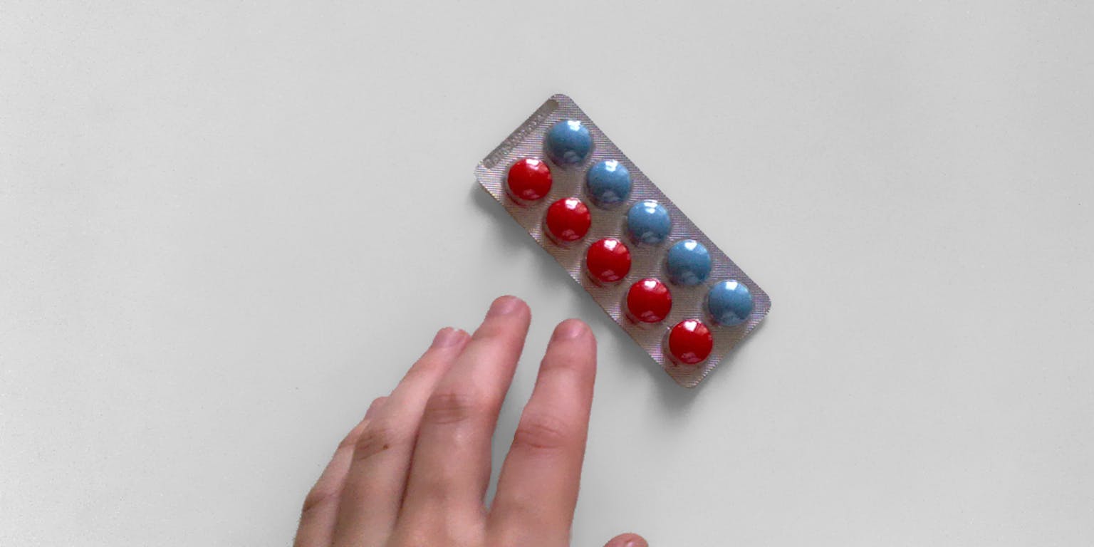 Een pillenstrip met blauwe en rode pillen. Een hand reikt naar de pillenstrip. De achtergrond is wit.