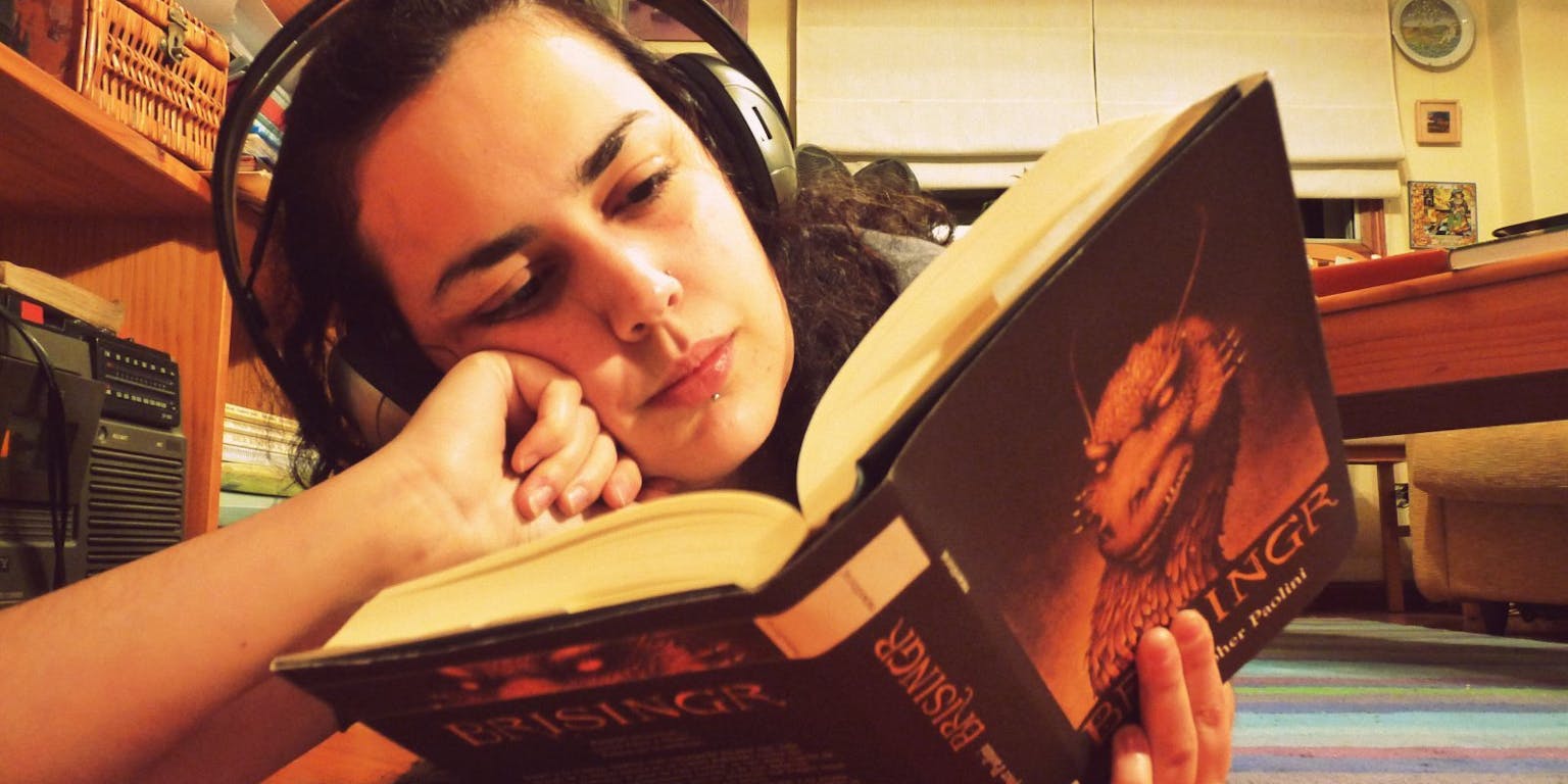 Een meisje met een koptelefoon leest een boek.