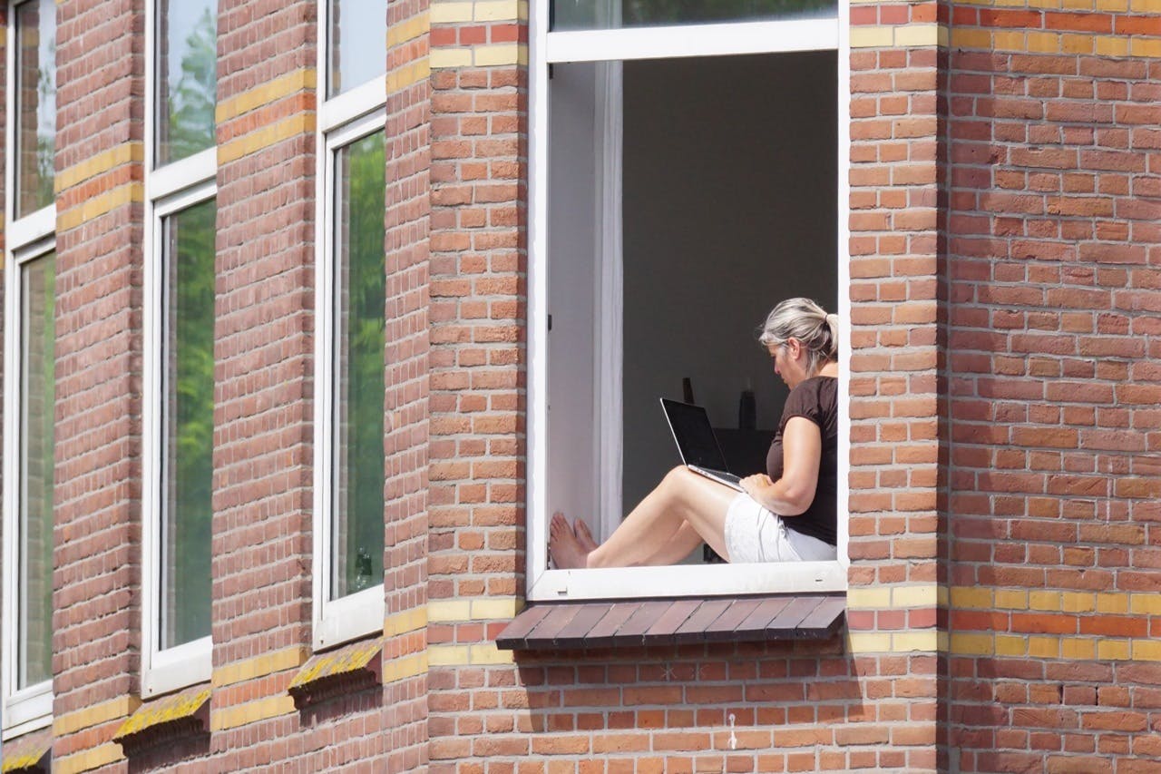 Een vrouw achter haar laptop voor het raam