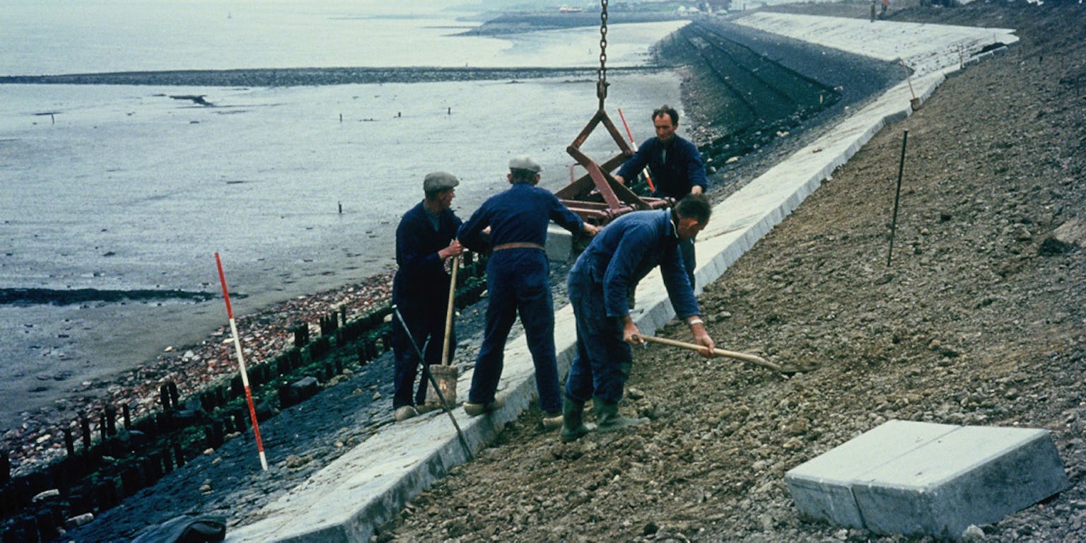 Vier personen die aan het werk zijn om de dijk van de Westerschelde te versterken.