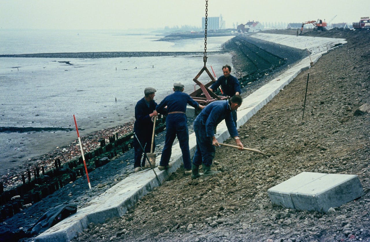Vier personen die aan het werk zijn om de dijk van de Westerschelde te versterken.