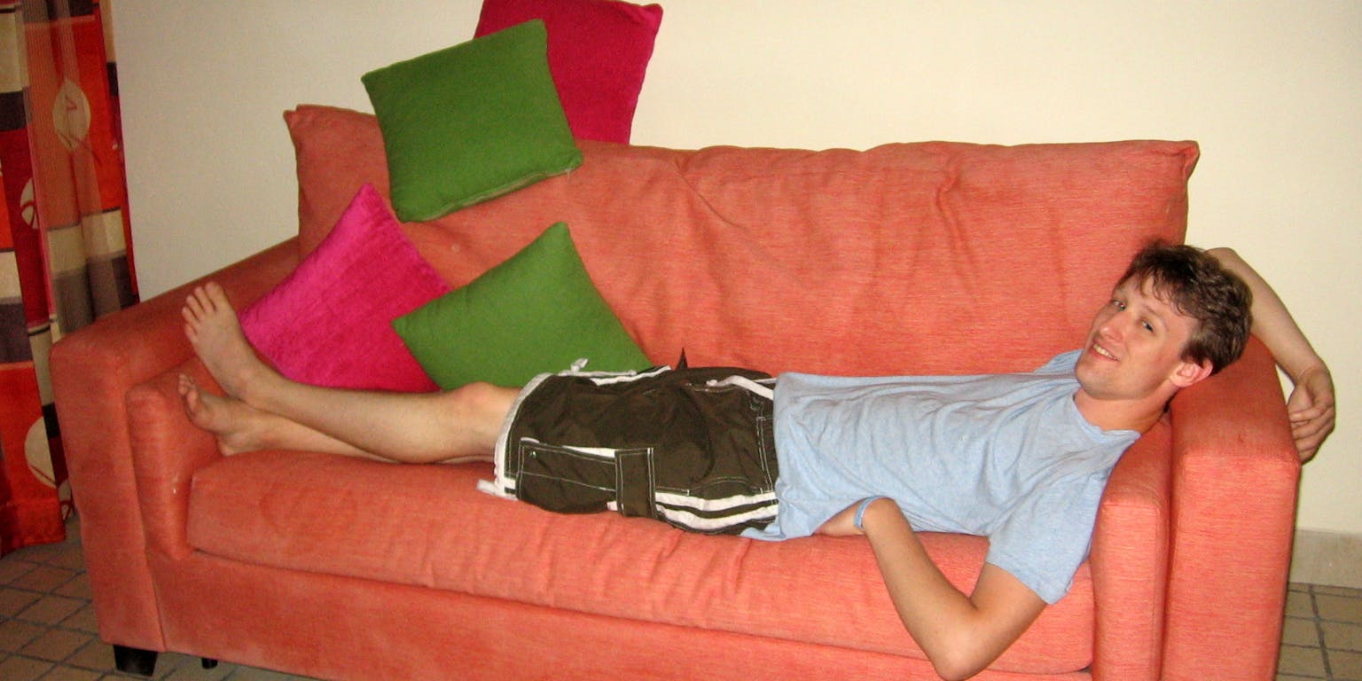 Een persoon die in zijn korte broek en t-shirt op een koraalkleurige bank ligt.