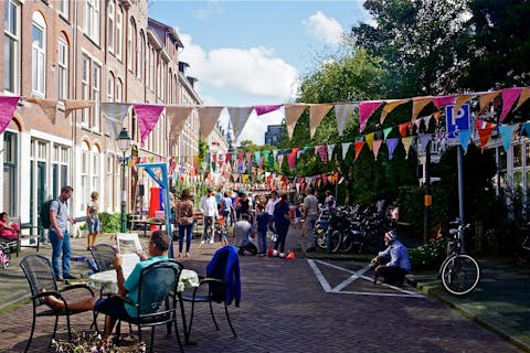 Het organiseren van een straatfeest zegt nauwelijks iets over hoeveel de deelnemers met elkaar hebben. Een straat versierd met vlaggetjes. Buurtbewoners zitten en staan op straat tijdens een buurtfeest.