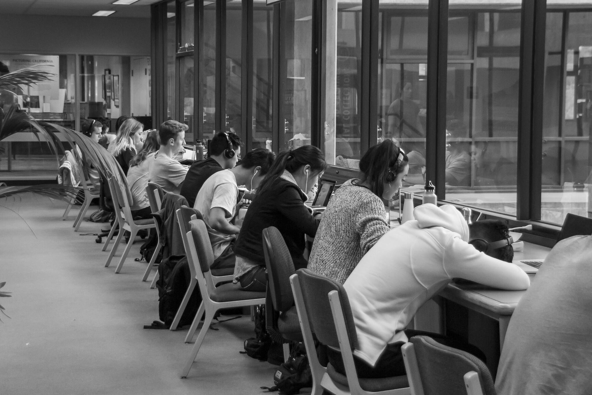 Een zwart-witfoto van studenten die aan een lange tafel in een bibliotheek zitten.