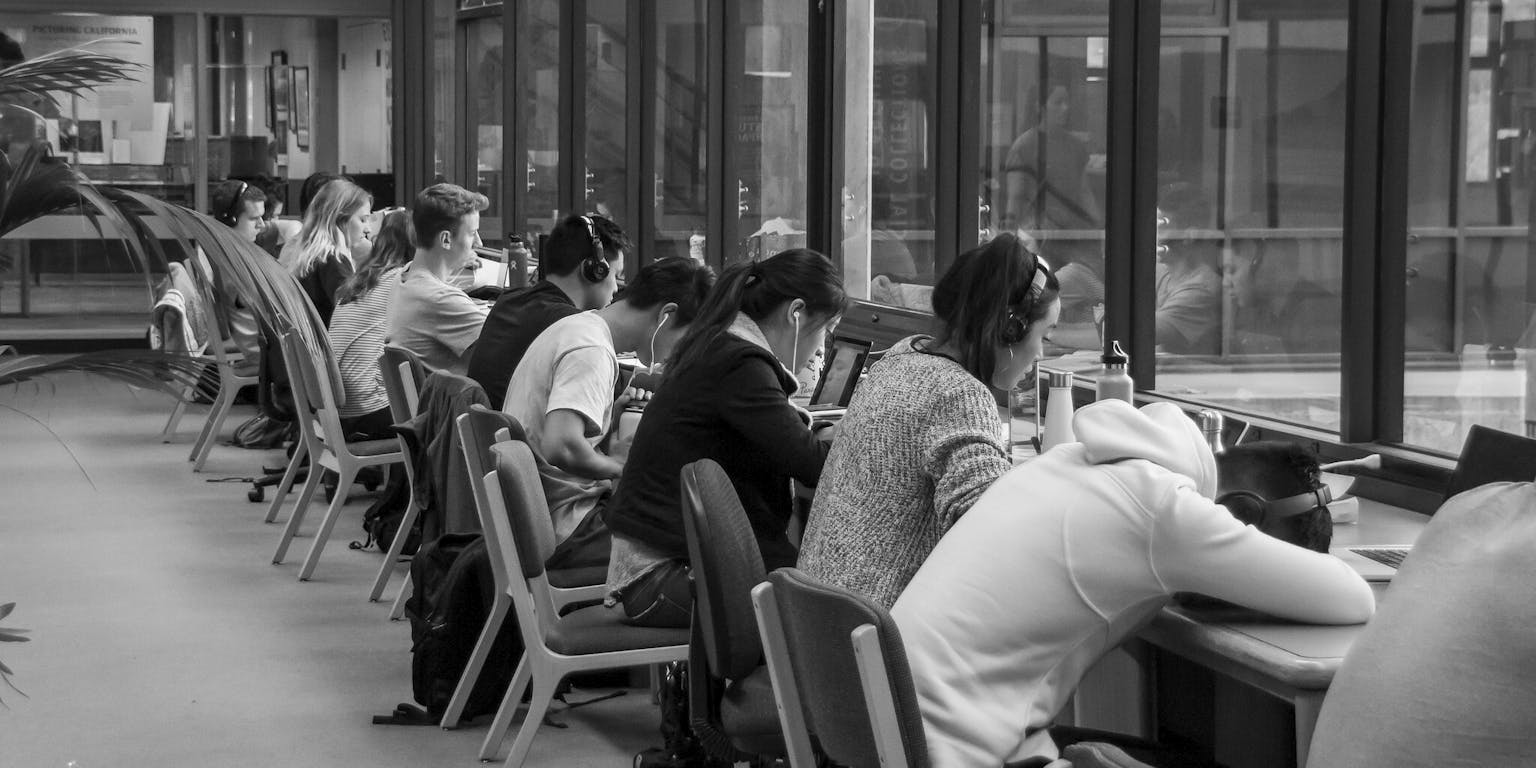Een zwart-witfoto van studenten die aan een lange tafel in een bibliotheek zitten.