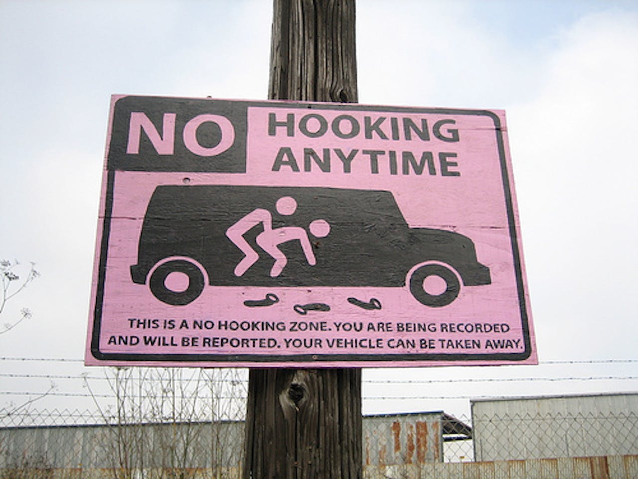 Een roze waarschuwingsbord op een paal. Prostitutie is verboden. De auto kan worden weggesleept.