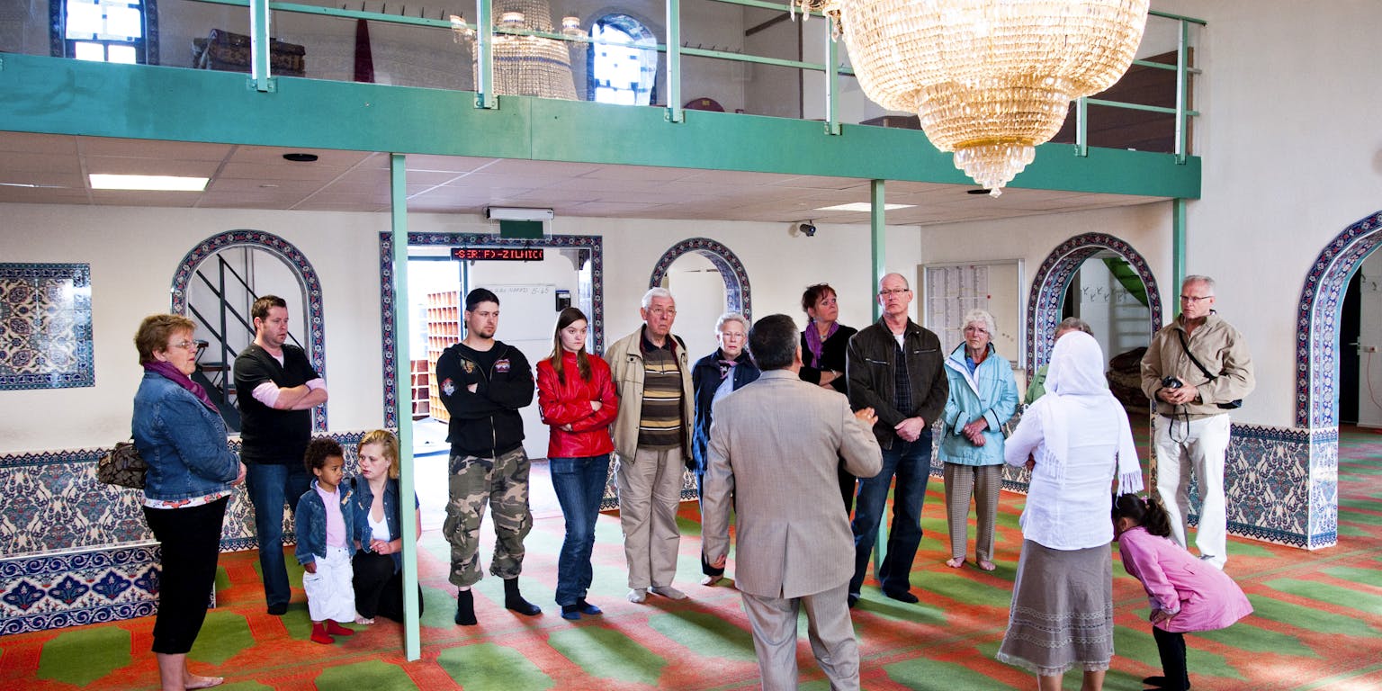 Een groep mensen staat in een moskee met een kroonluchter.