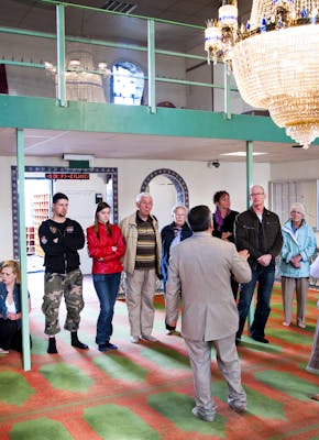 Een groep mensen staat in een moskee met een kroonluchter.