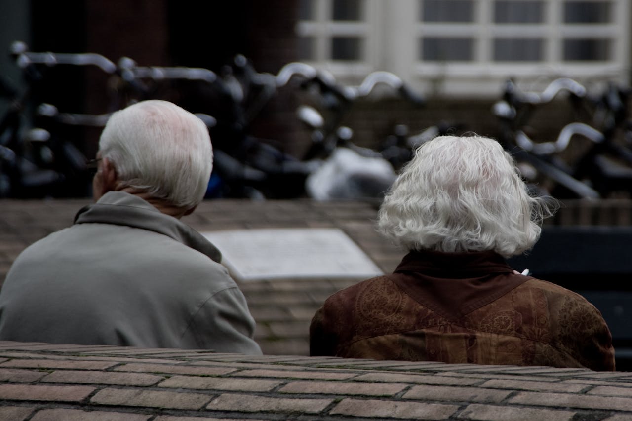 Een ouder echtpaar zit samen op een bankje. De foto is vanaf de achterzijde genomen.