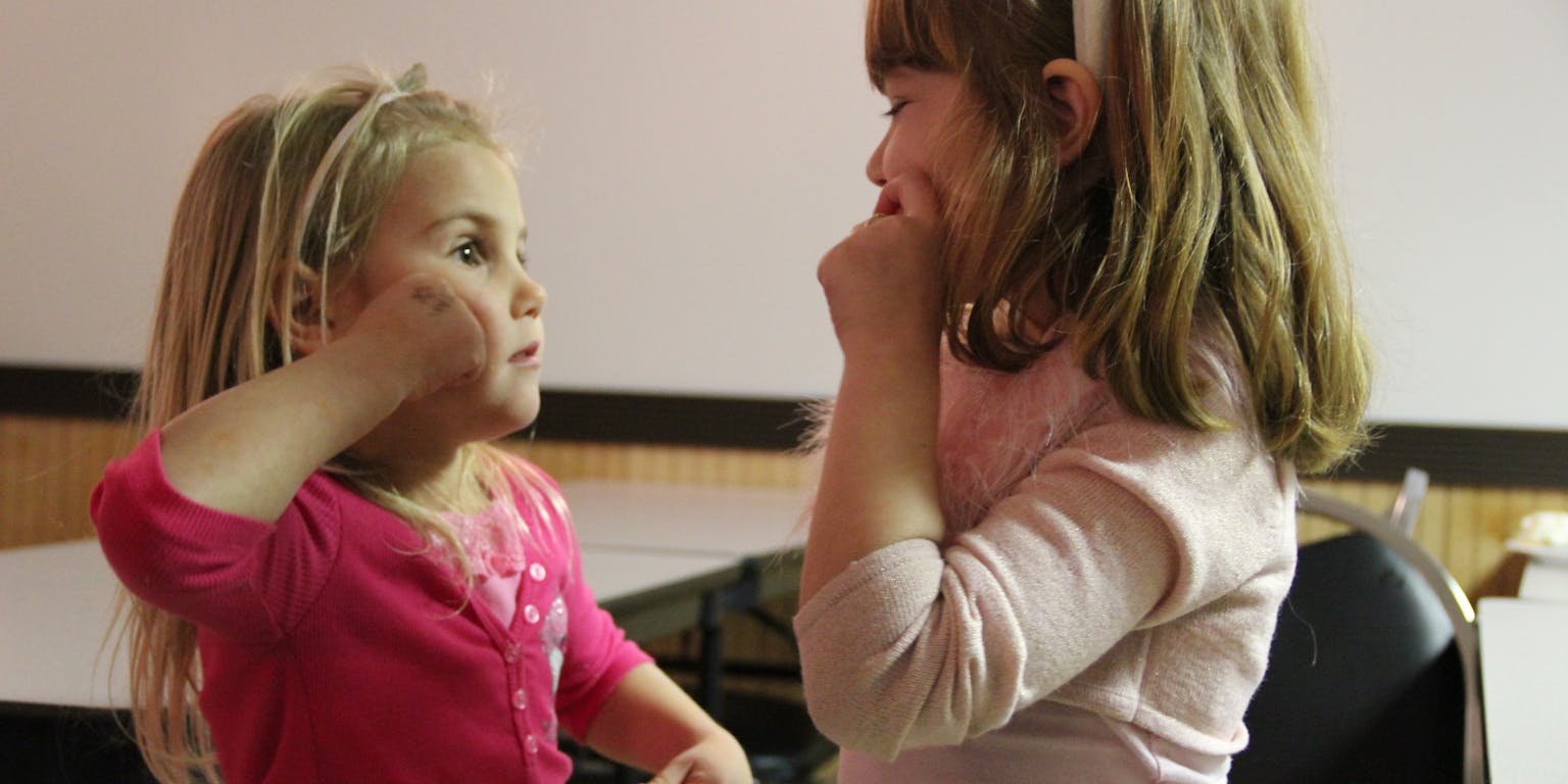 Twee kleine meisjes gebaren naar elkaar aan in een kamer.