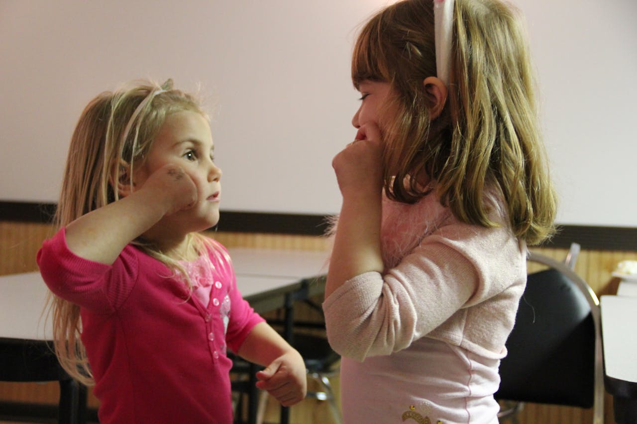 Twee kleine meisjes gebaren naar elkaar aan in een kamer.