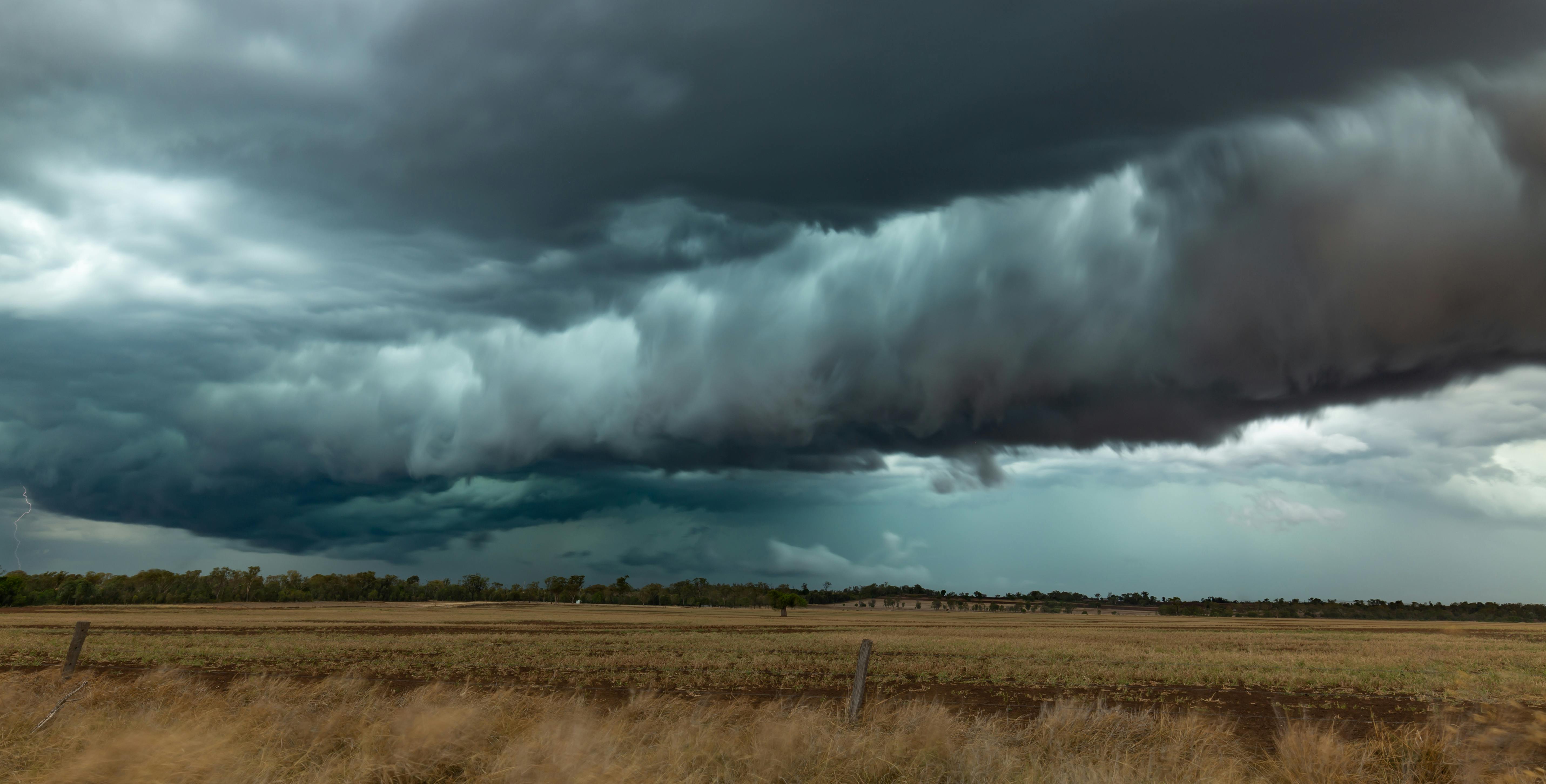 Een dreigende, grijze wolkenlucht boven een bruin graslandschap.
