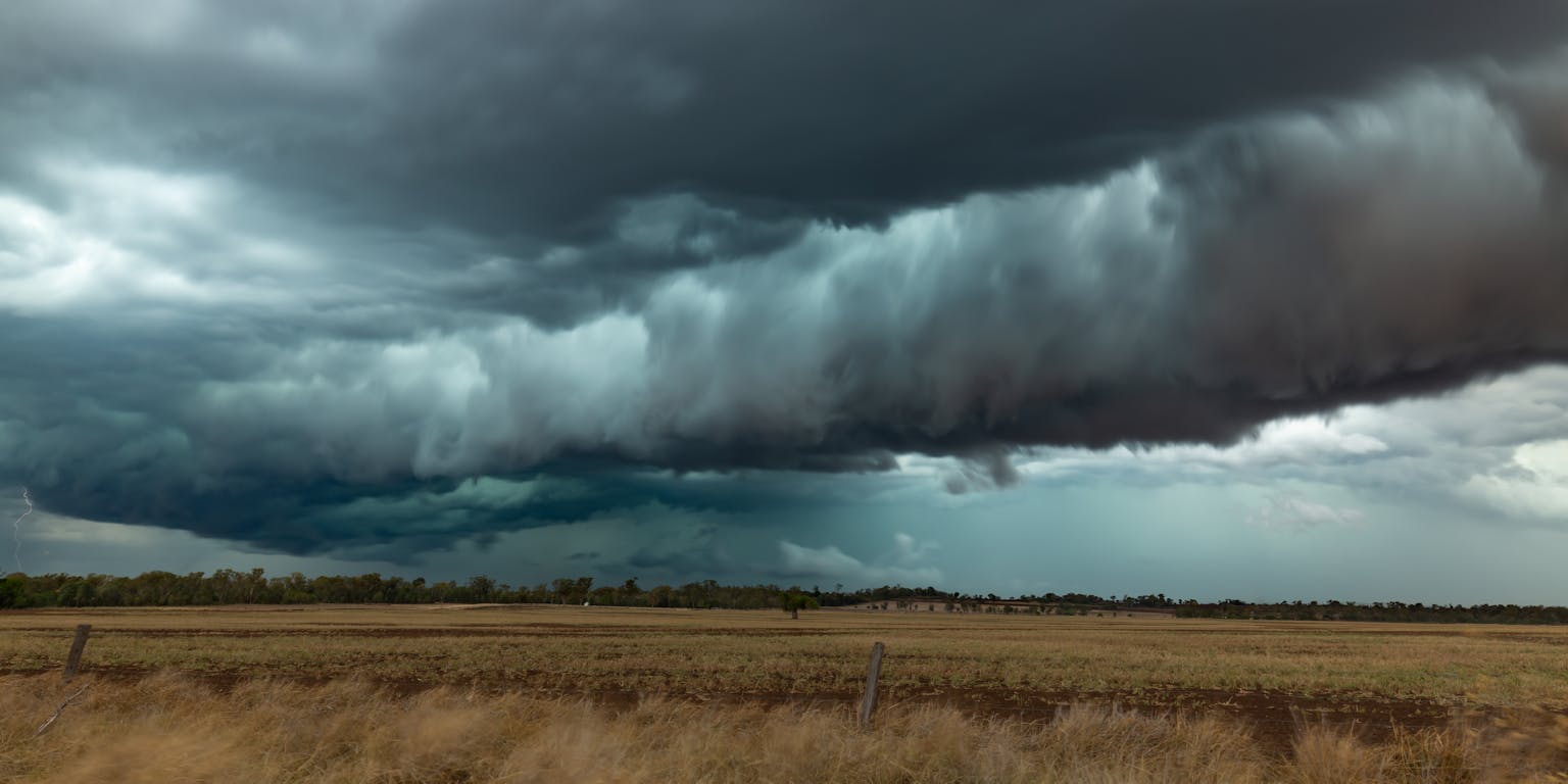Een dreigende, grijze wolkenlucht boven een bruin graslandschap.