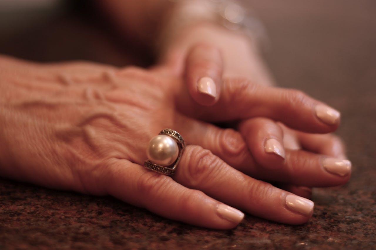 De handen van een vrouw met een parelring erop. De nagels zijn zachtroze gelakt.