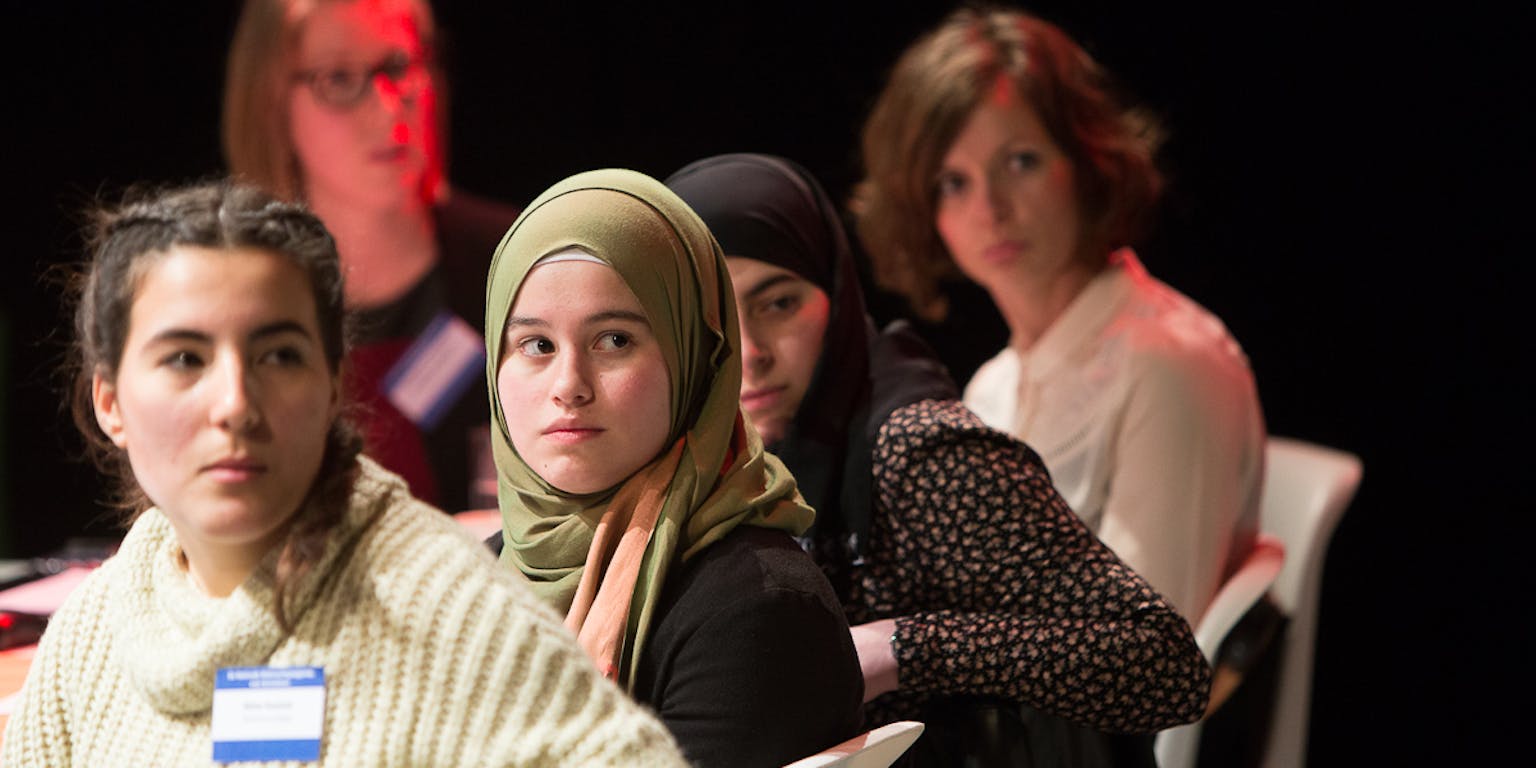 Een groep vrouwen zit aan een tafel en luistren aandachtig.