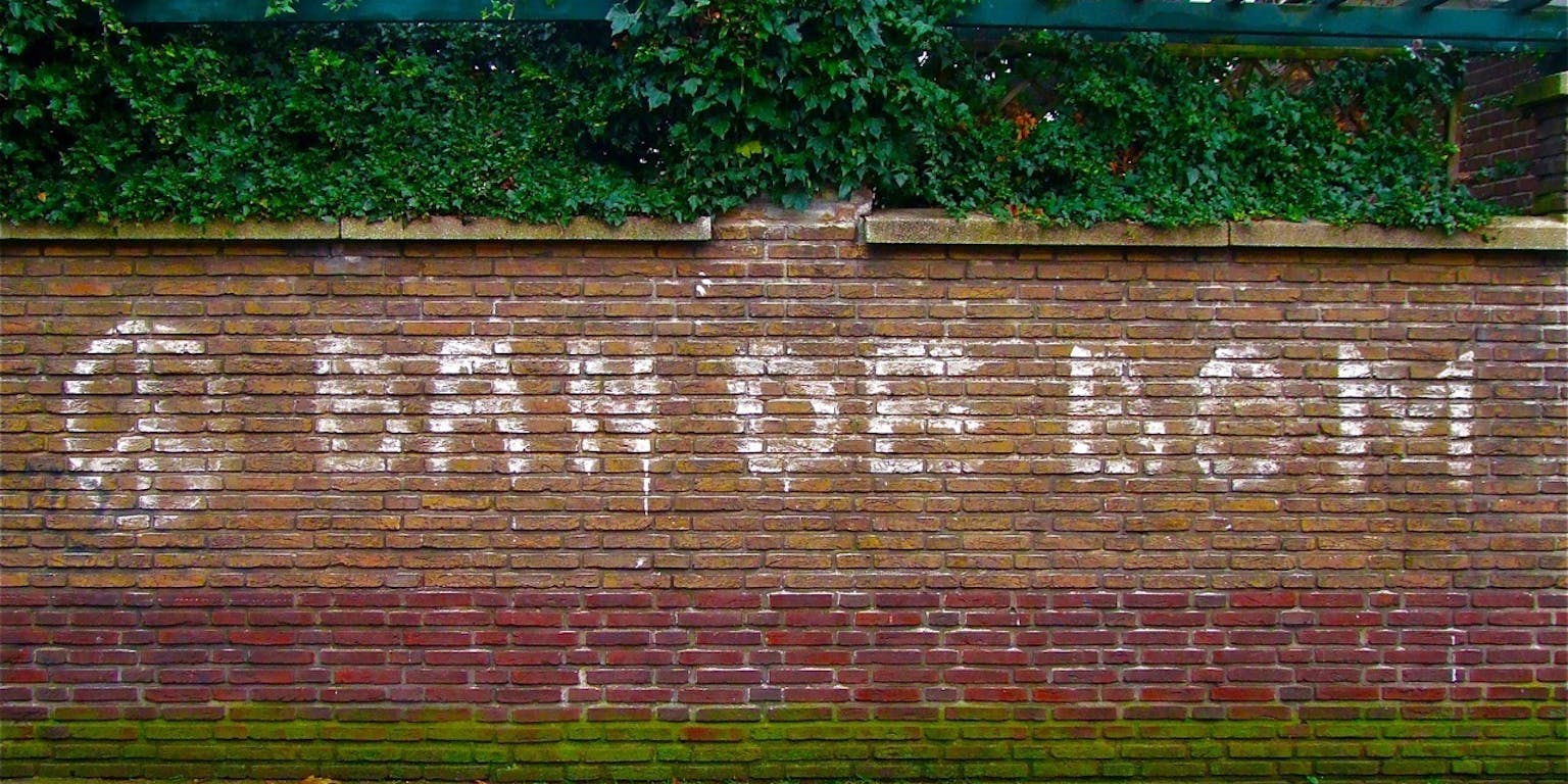 Ban de bom' met graffiti op een muur geschreven. Ook is het teken van vrede erop gespoten.