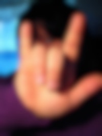 Een vrouw in een paarse trui met zwart haar, laat een 'rock and roll' teken zien met haar hand.